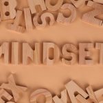 Wooden alphabet letters arranged to spell 'Mindset' on a peach background.